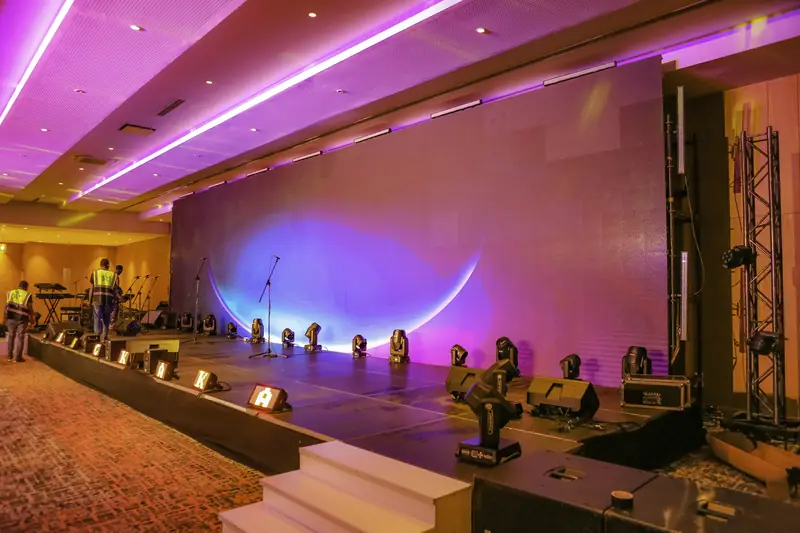 Ballroom stage set with moving-head lights, truss and a lit backdrop before an event