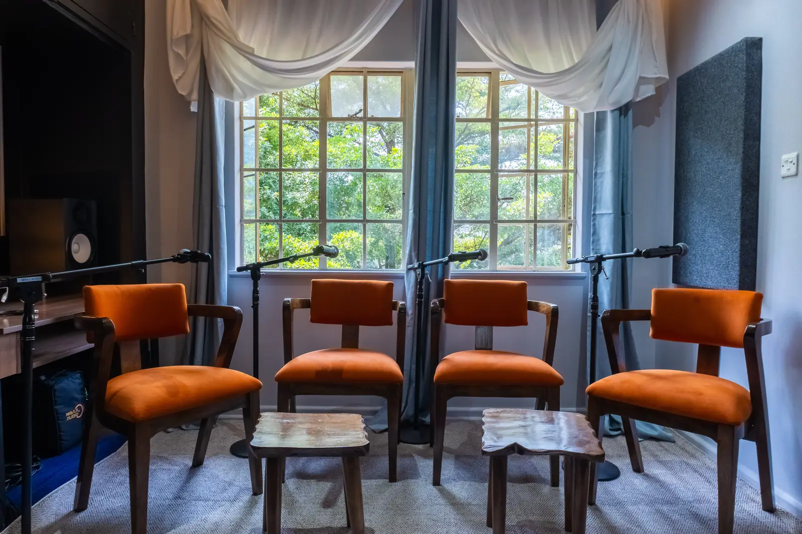 Santoori podcast room with four orange upholstered chairs, microphones on stands and acoustic panels