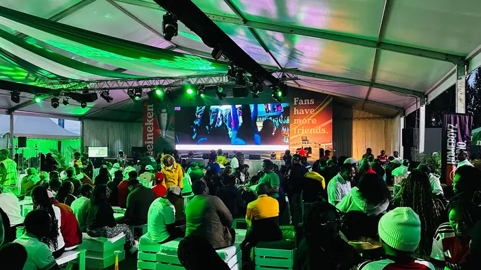 Fans watching a large screen under green stage lighting at the Heineken screening