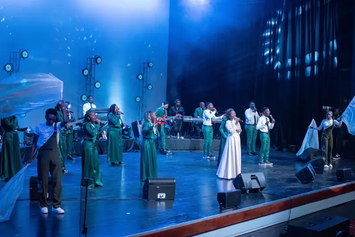 Choir and band performing on a blue-lit stage during a live recording